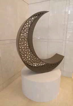 Decorative crescent moon sculpture with geometric cutouts on white pedestal