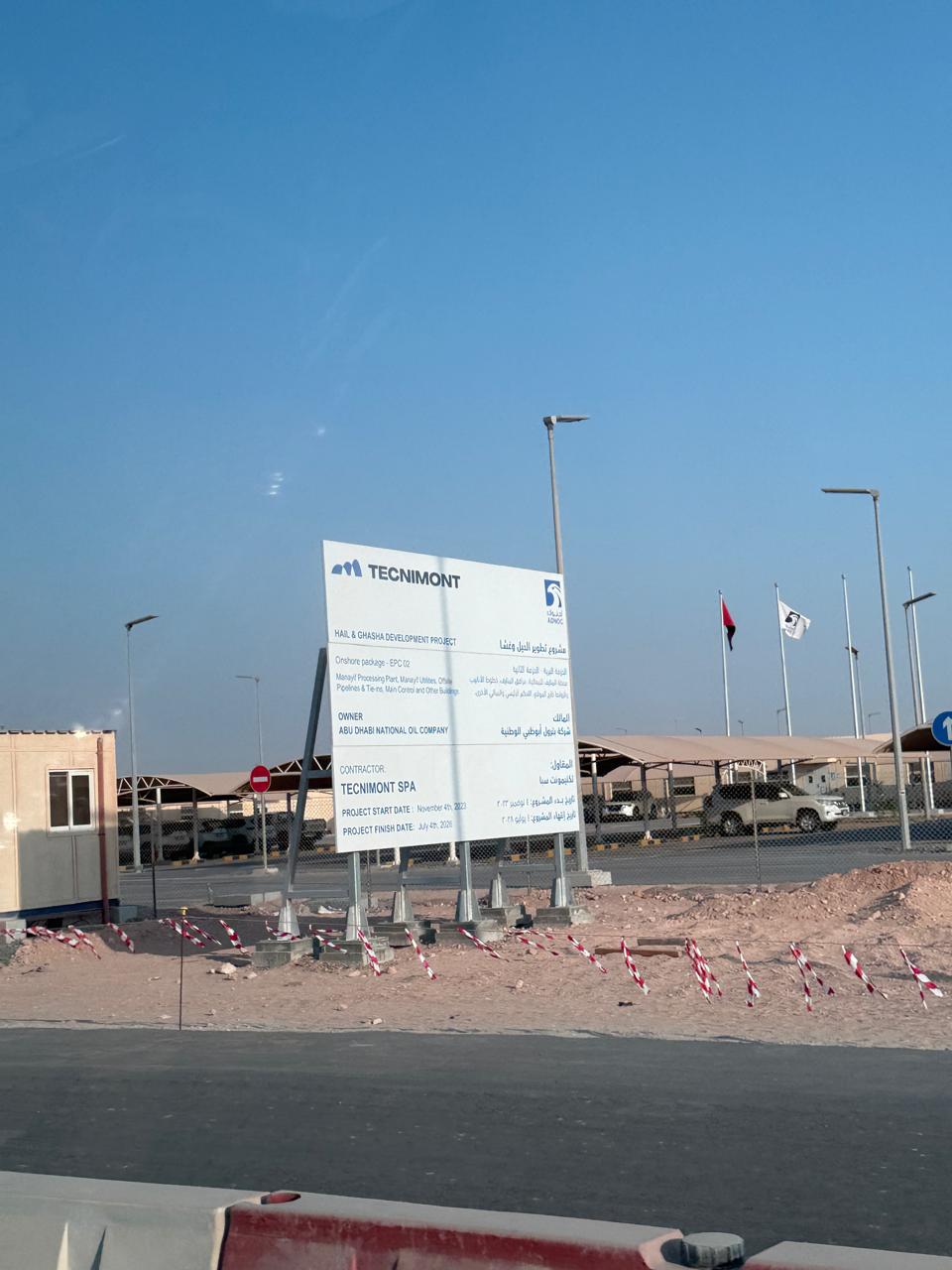 Large white construction site sign structure beside road